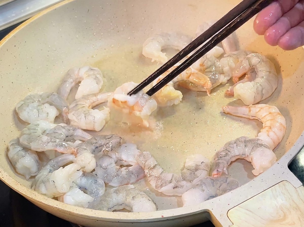 기름을 두른 프라이팬에서 핑크빛으로 익은 새우를 나무젓가락으로 뒤집는 모습.