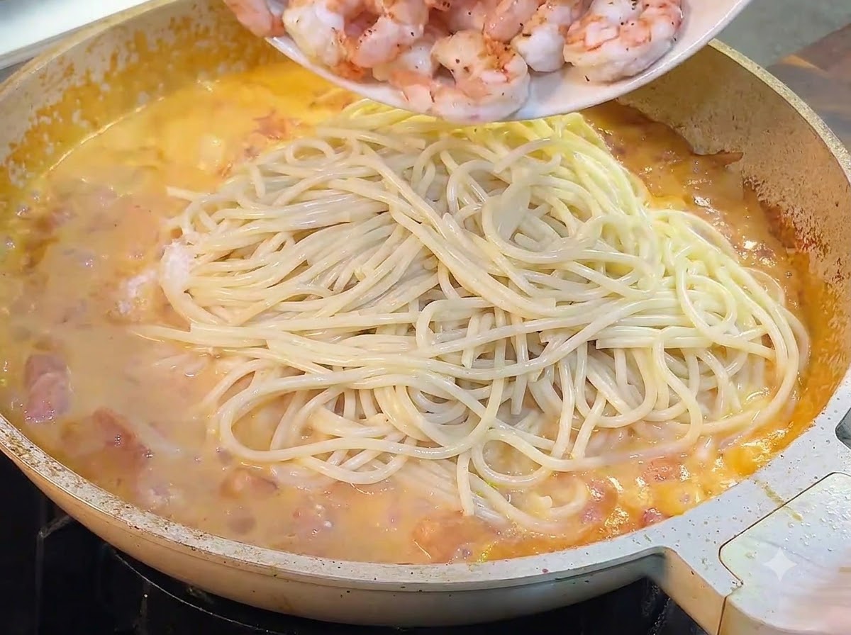 접시에 담아둔 익은 새우를 파스타 면과 소스가 있는 팬에 붓는 모습.