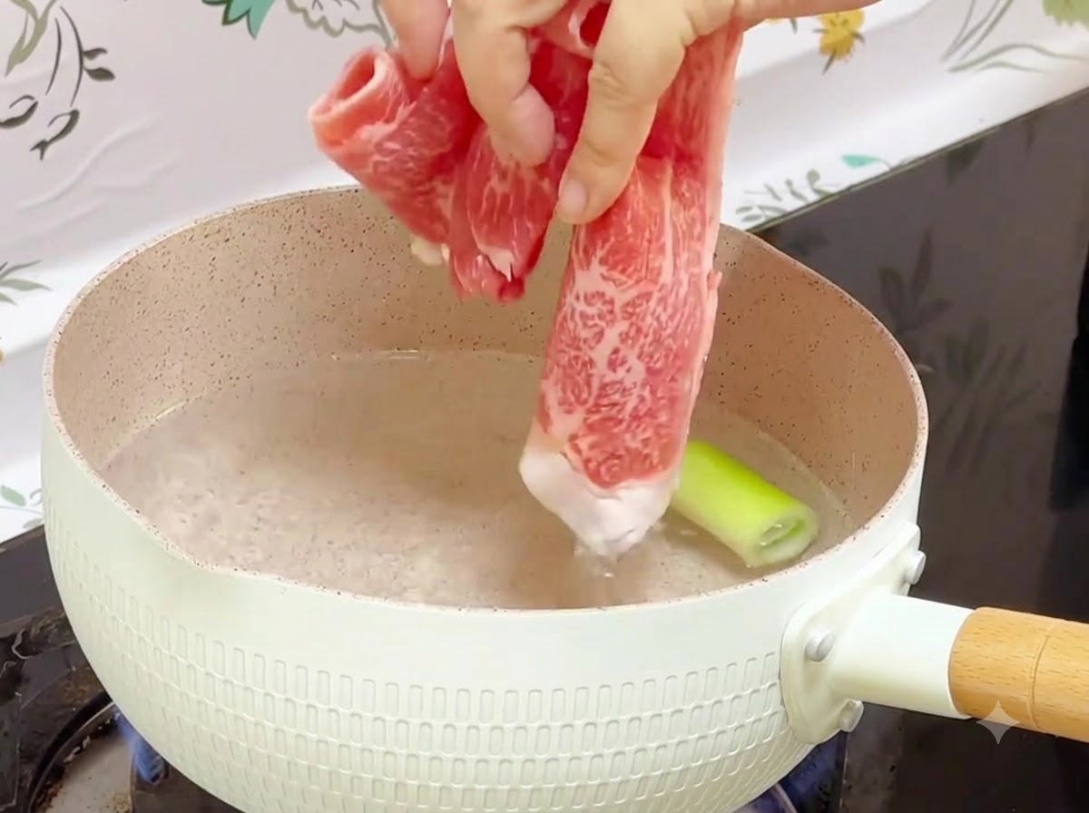 대파 조각이 들어간 끓는 물에 냉동 소고기 롤을 넣고 있는 모습