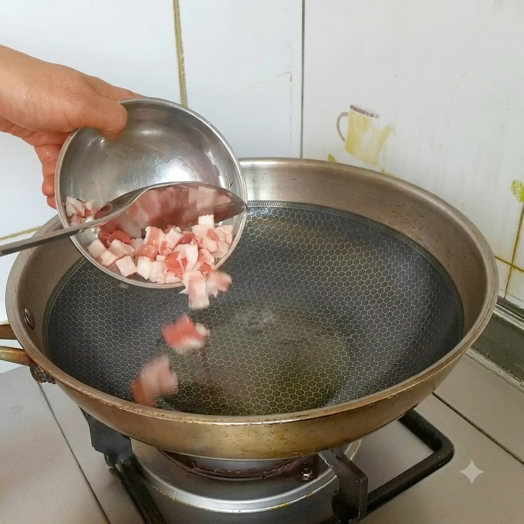 달궈진 스테인리스 웍에 기름을 두르고 작은 그릇에 담긴 깍둑썰기한 삼겹살을 넣는 모습.