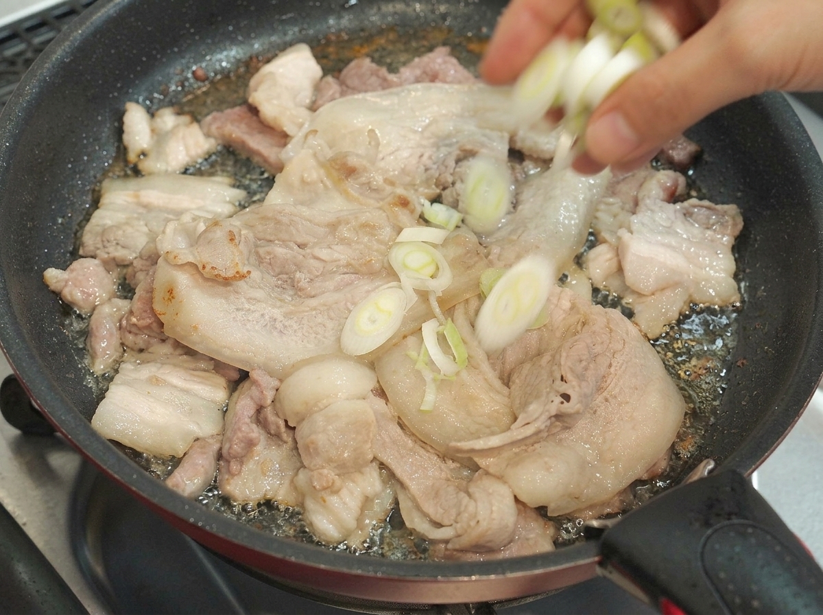 조리 중인 돼지고기 삼겹살 팬에 다진 대파를 넣고 있는 모습.