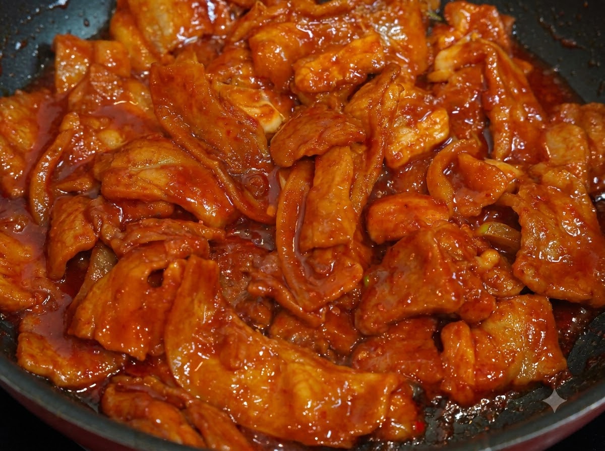 팬에 조리된 매콤한 돼지고기 위에 하얀 참깨가 뿌려져 있는 클로즈업 샷.