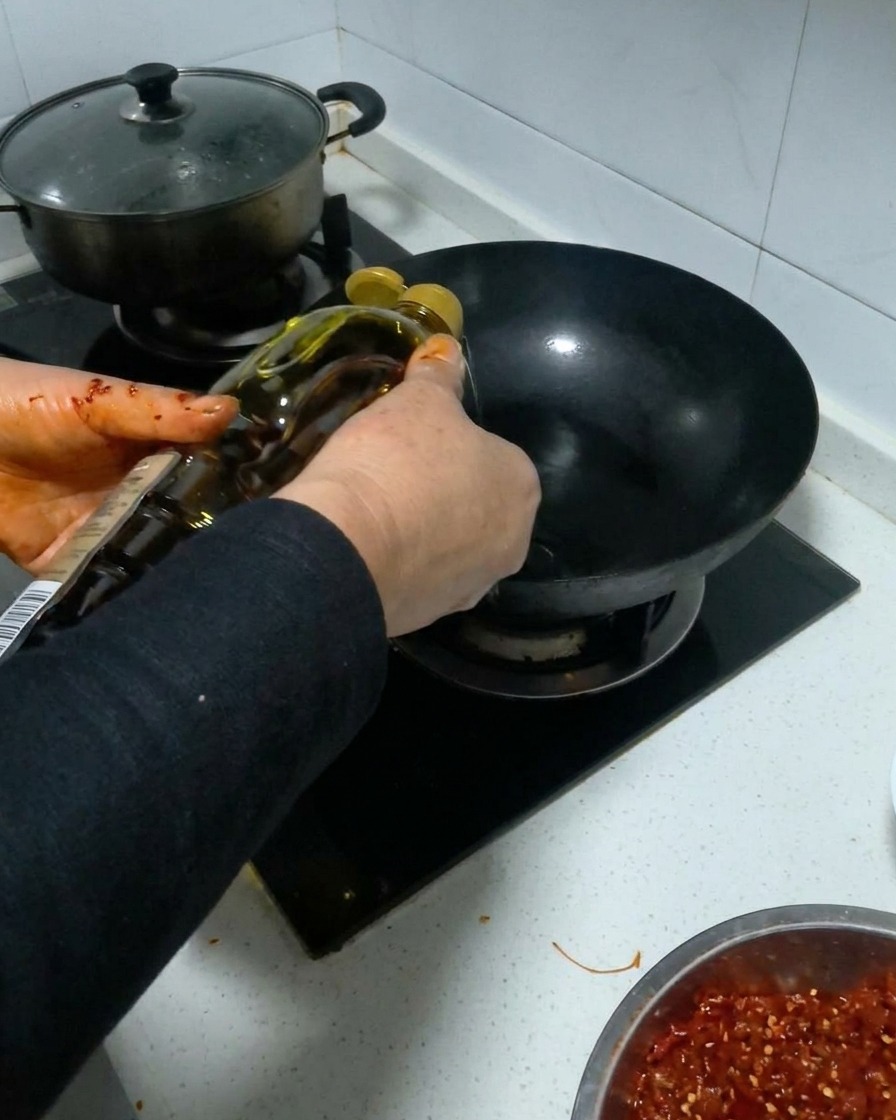 달궈진 검은 웍에 병에 든 식용유를 붓는 모습.