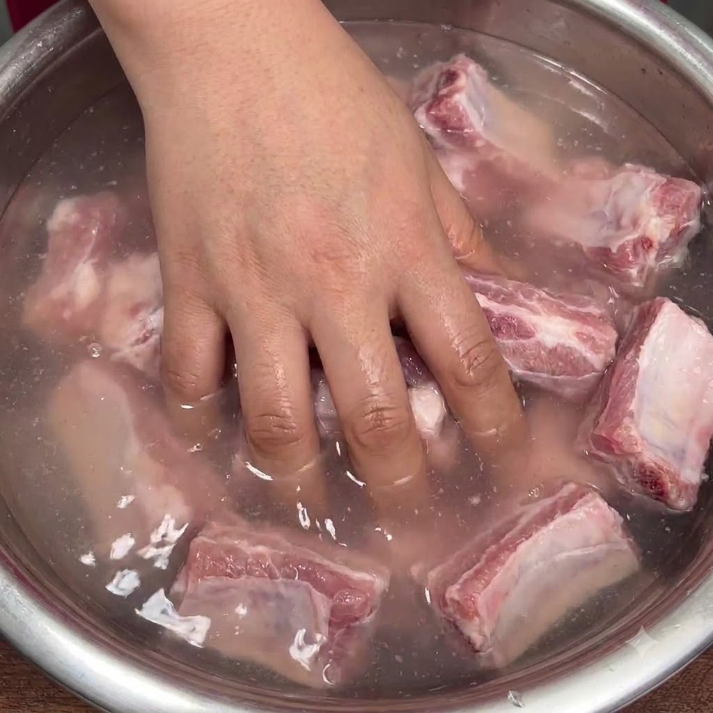 뿌연 물이 담긴 그릇 안에서 손으로 생 돼지갈비를 활기차게 섞는 모습.