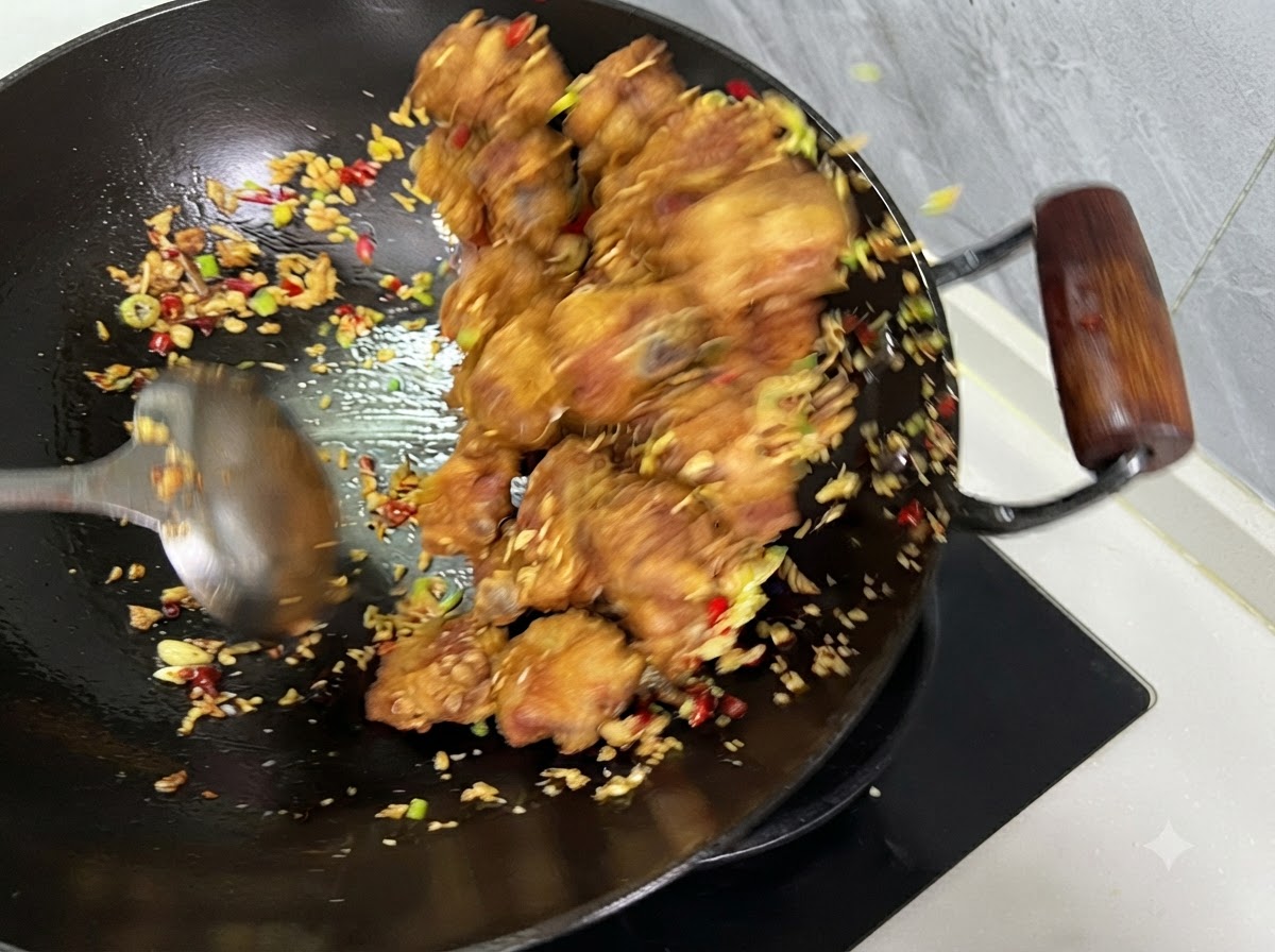 웍 안에서 국자로 갈비, 고추, 마늘이 함께 섞이도록 볶아지는 모습.