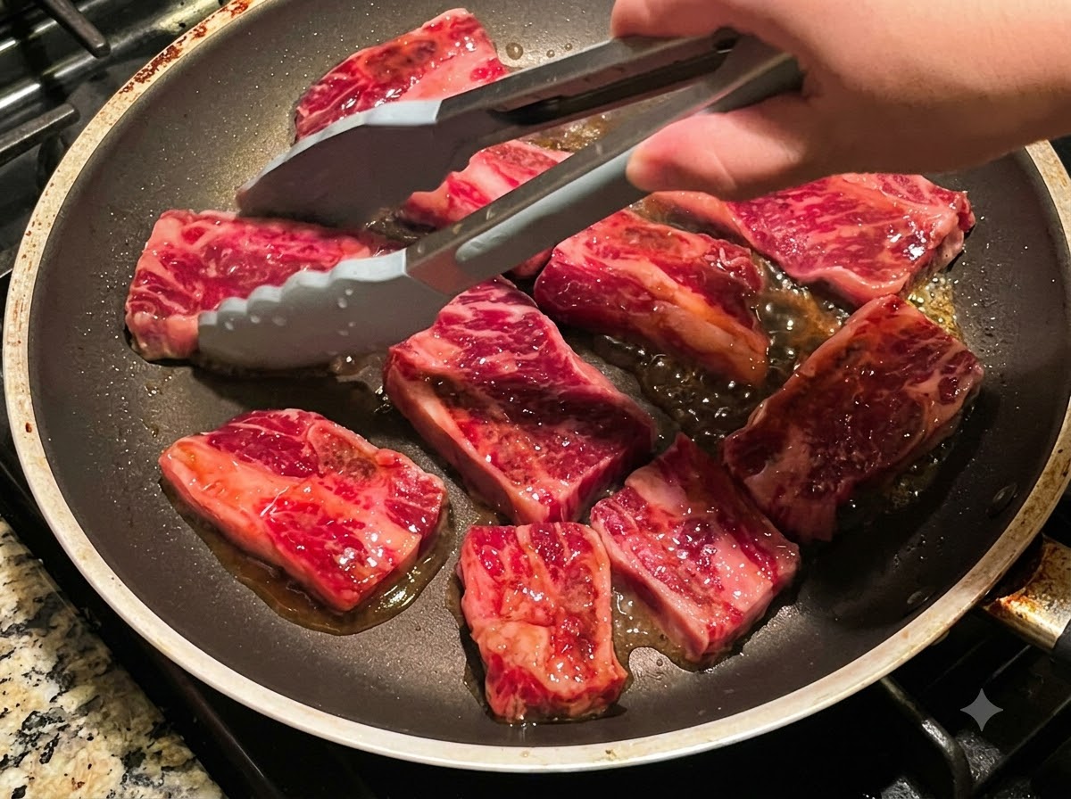 팬에서 익어가고 있는 소갈비를 집게로 여러 조각 뒤집는 모습.