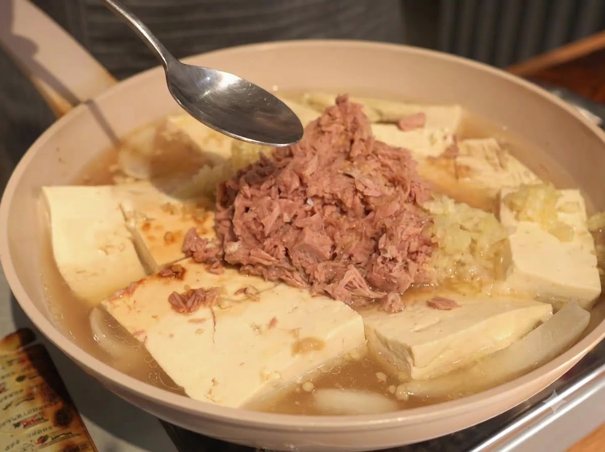 참치와 두부가 담긴 냄비에 각종 조미료와 고춧가루를 올리는 모습.