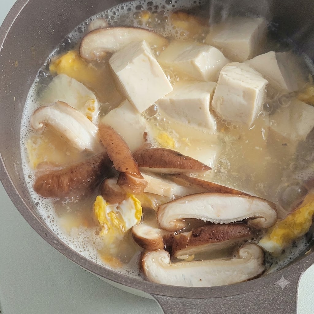 버섯, 구운 달걀 조각과 함께 맛있는 육수 속에서 끓고 있는 부드러운 하얀 두부 큐브.