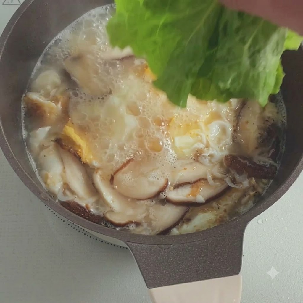 버섯과 달걀이 끓고 있는 냄비 속으로 신선한 상추 잎이 들어가는 모습.