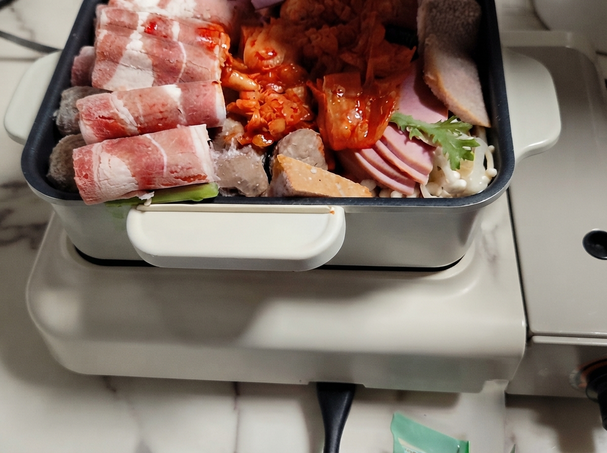 고기, 채소, 떡이 층층이 세팅된 핫팟에 육수가 부어지는 모습.