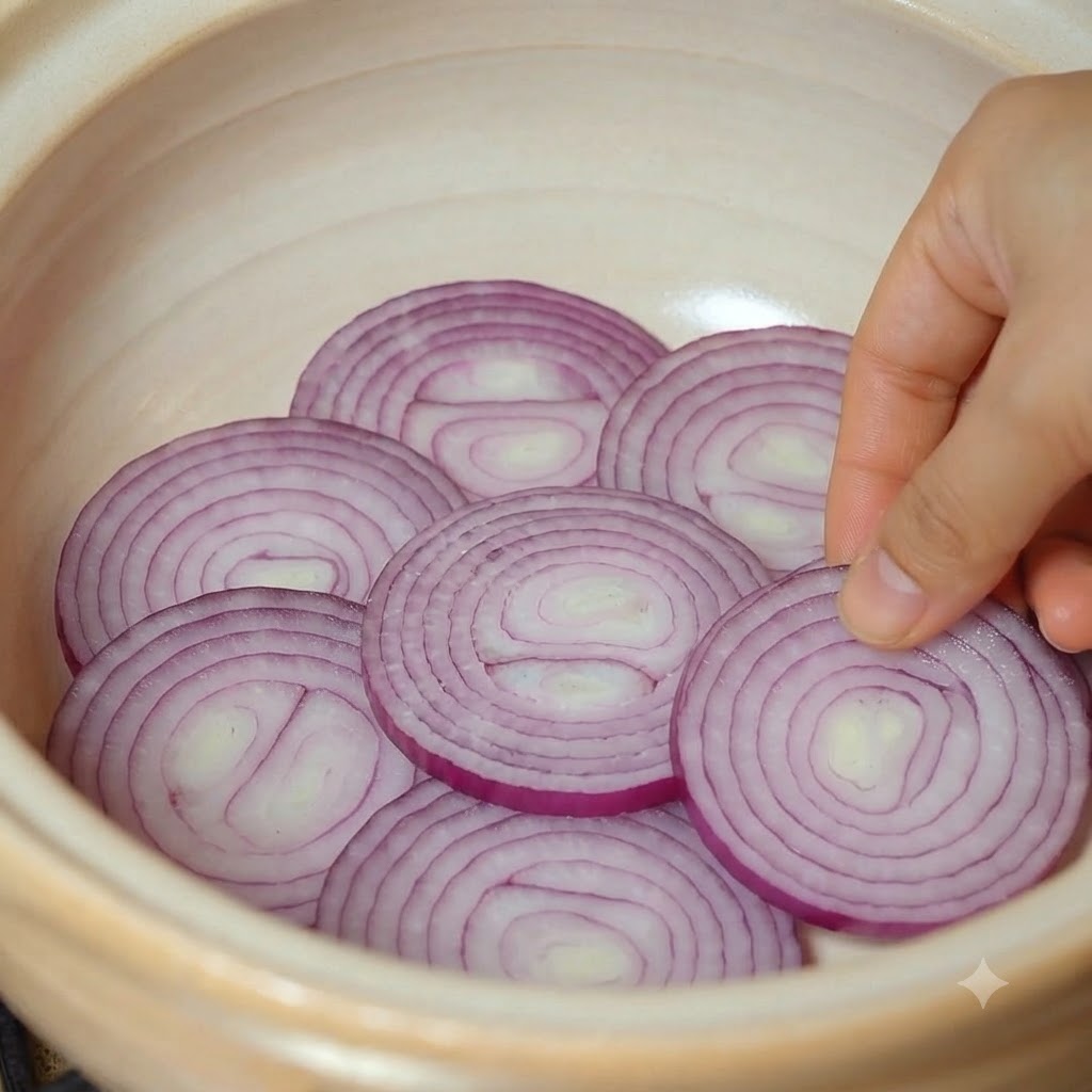 뚝배기 냄비 바닥에 썬 적양파 조각들을 가지런히 정리해 담는 모습.