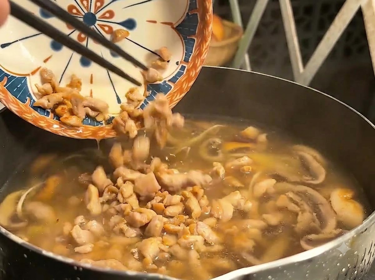 무늬가 있는 접시에 담겼던 익힌 돼지고기 조각을 젓가락으로 끓는 국수 냄비에 밀어 넣는 모습