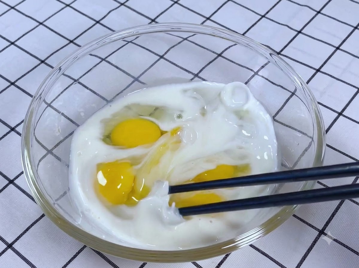 젓가락으로 유리 볼 안의 달걀, 우유, 소금, 설탕 혼합물을 철저히 젓는 모습.