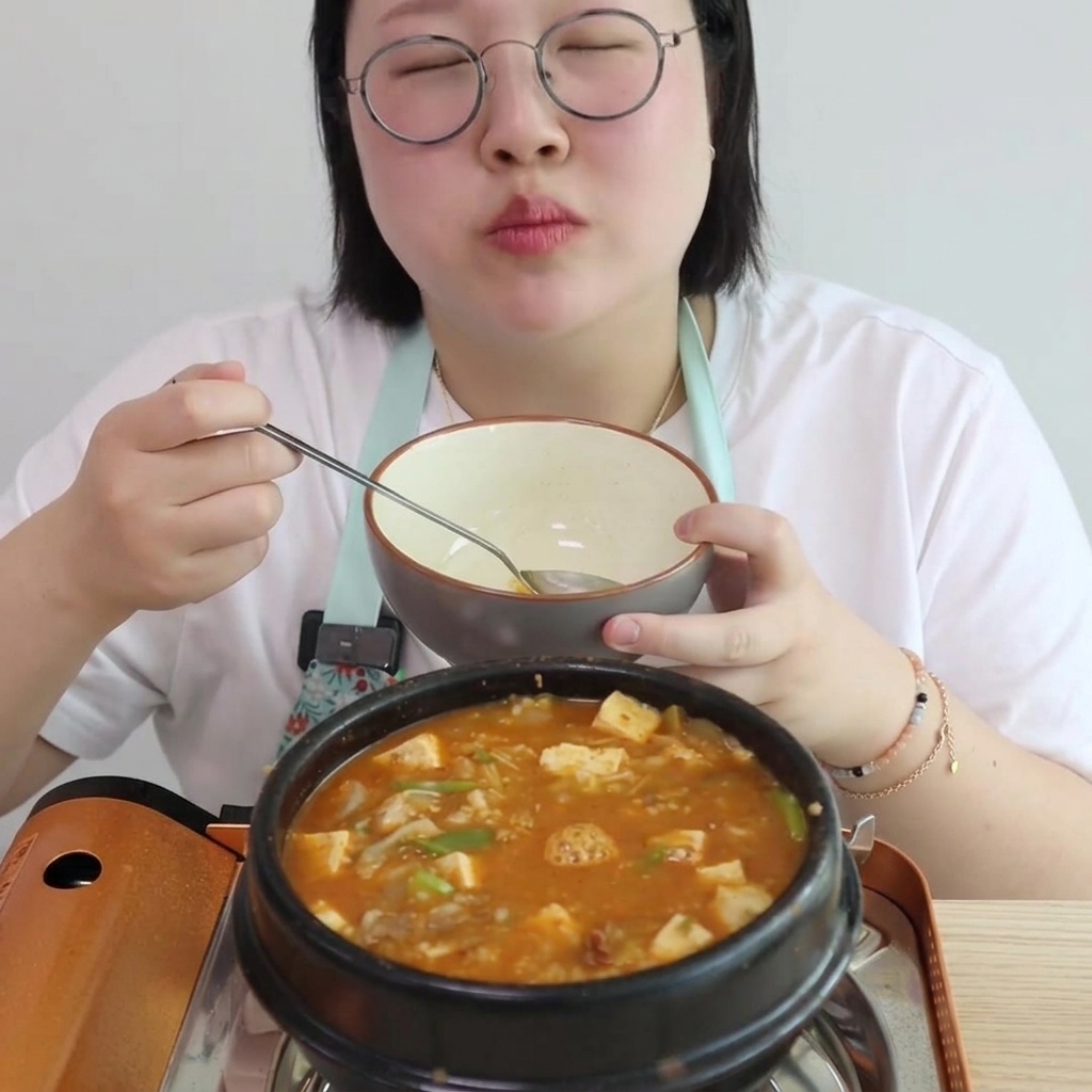 서빙 볼을 든 채 양념되어 볶아진 소고기와 페이스트가 담긴 냄비에 물을 붓고 있는 사람의 모습.