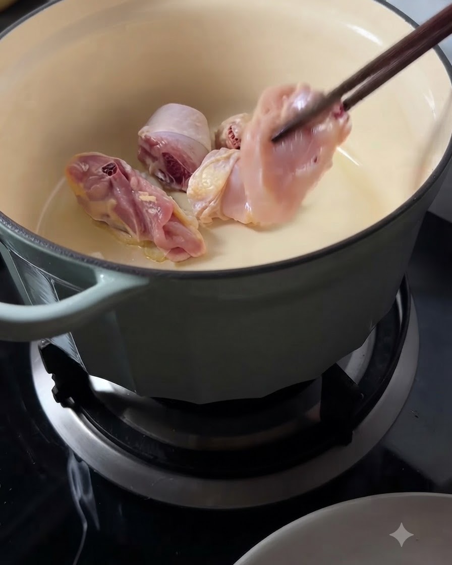 긴 나무 젓가락을 사용하여 달궈진 냄비에 생닭 조각들을 넣고 있는 모습.