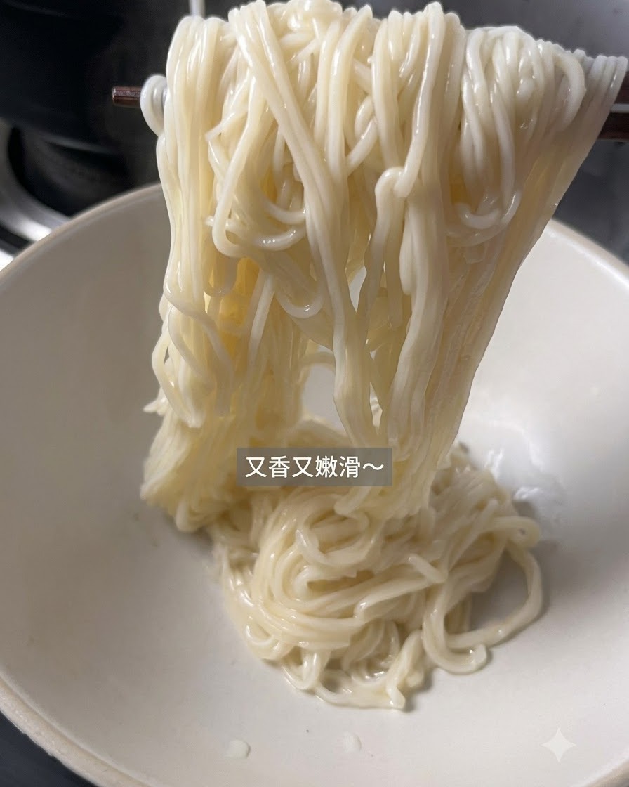 익은 면이 젓가락에 들려 비어 있는 하얀 서빙 그릇으로 옮겨지고 있는 모습.